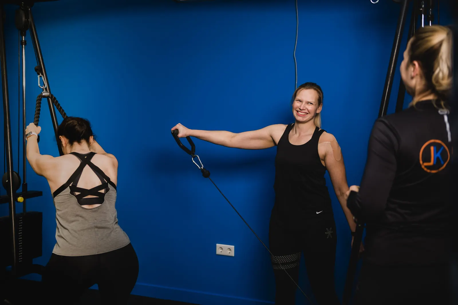 Twee deelnemers trainen aan de kabelmachine met begeleiding